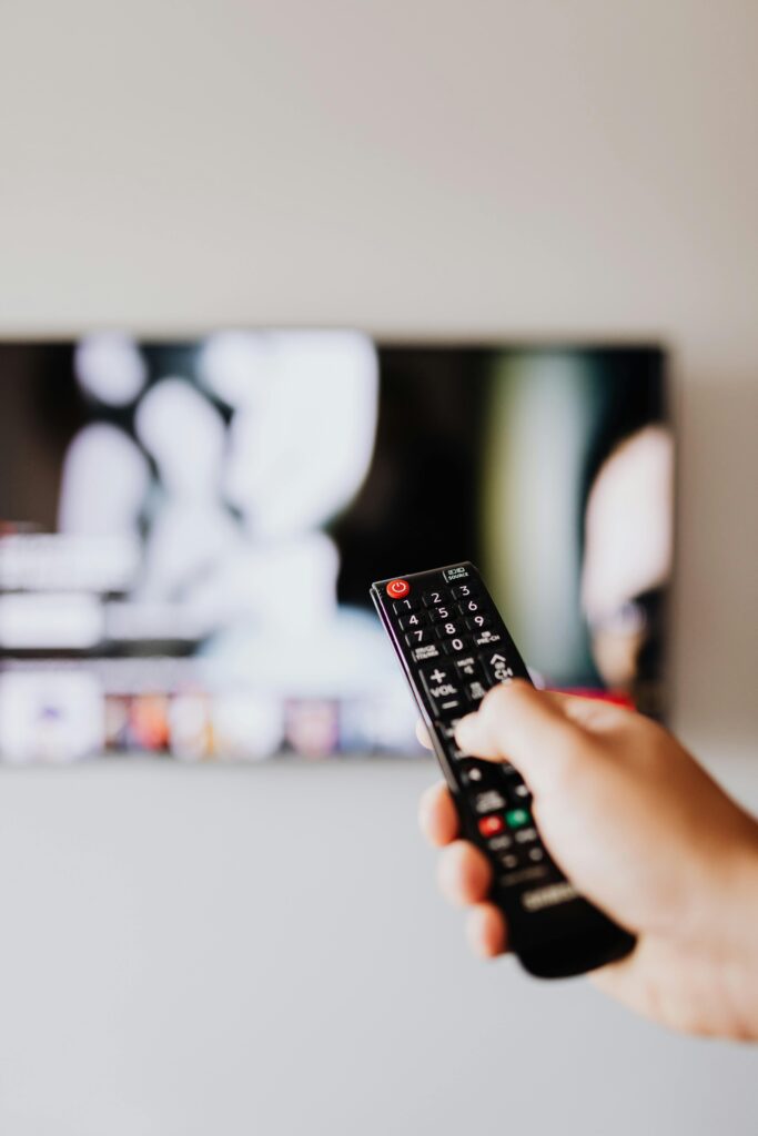 Close-up of a hand using a remote control to operate a TV with a blurred screen.